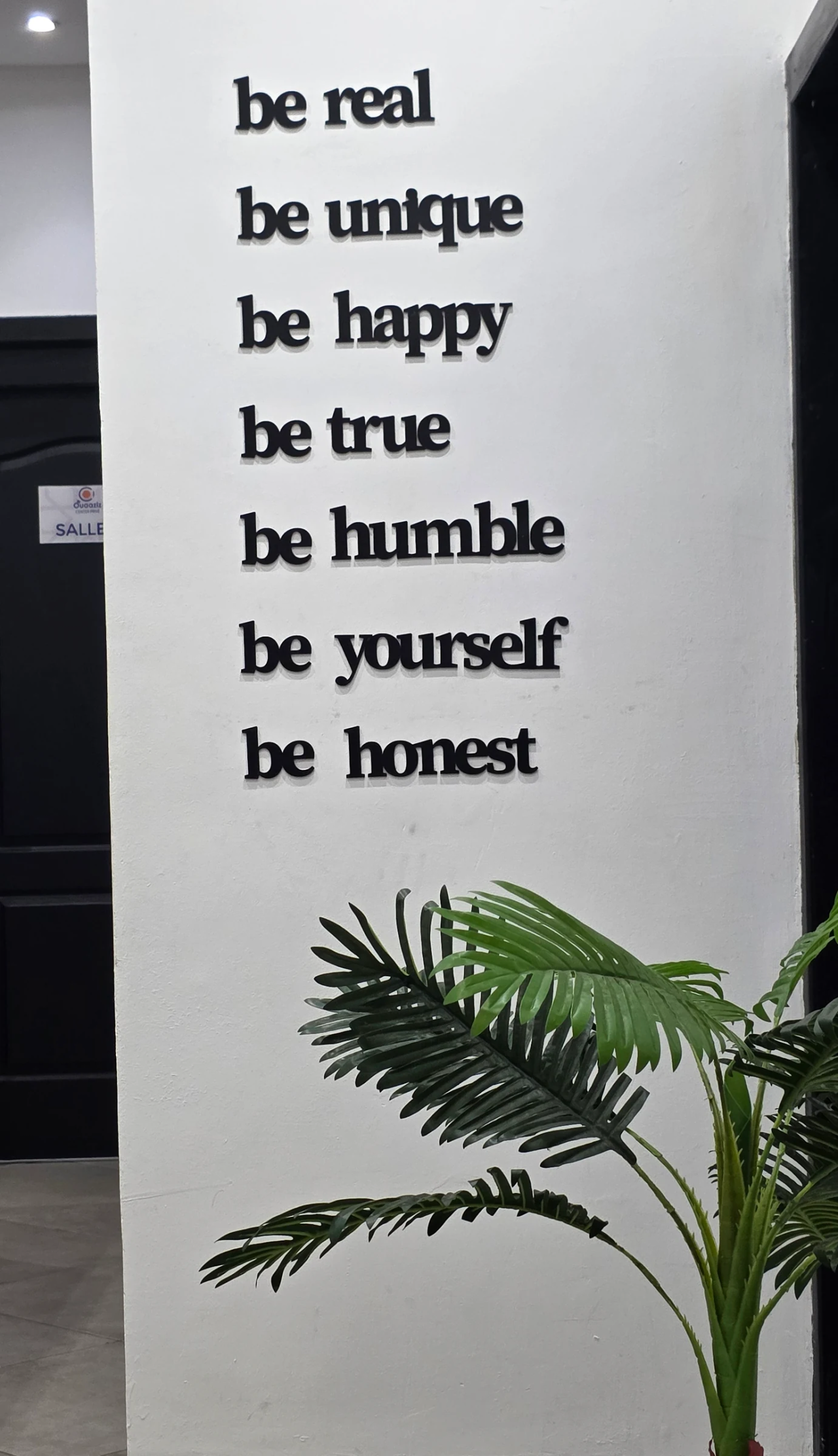 Les mots « be real, be unique » près d’une plante et des portes des salles.